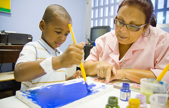 Menino pintando ao lado de uma senhora